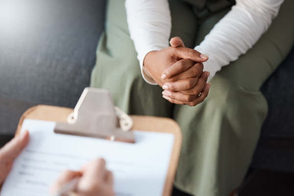 hands writing on clipboard across from person with clasped hands