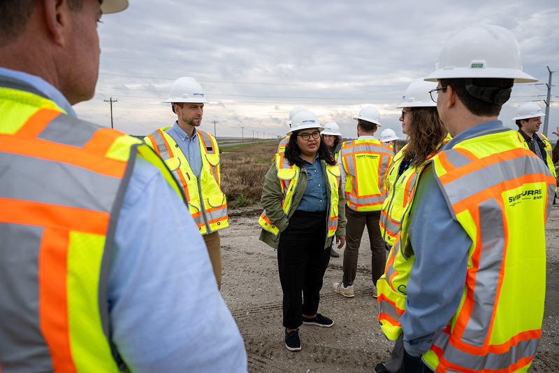 Group of people in safety gear having a discussion under a cloudy sky.