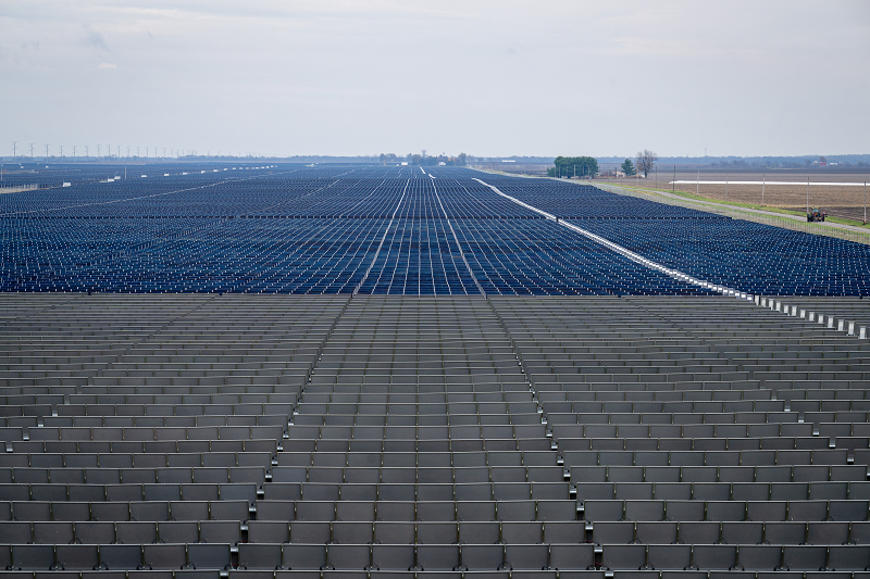 Vast solar farm with rows of photovoltaic panels extending towards the horizon under a cloudy sky.