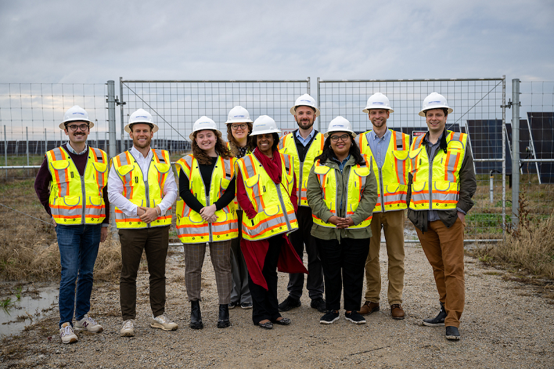 A group of City of Chicago employees wearing safety helmets and high-visibility vests stands in front of rows of solar panels.