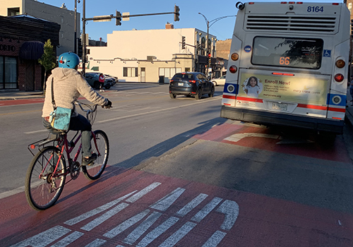 Person biking away from viewer behind CTA bus