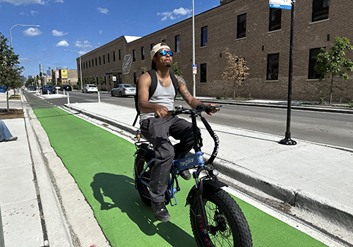 Person riding towards viewer on a blue Divvy bike in a bi-directional protected bike lane with concrete separating them from the vehicle travel lane