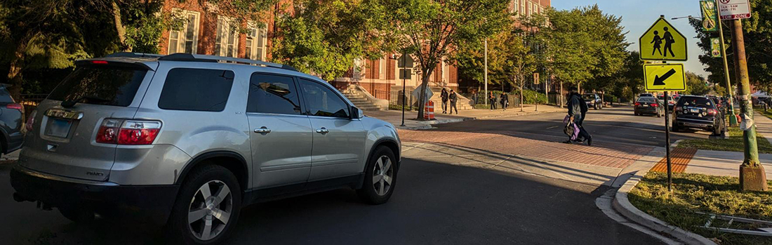 student crossing street in front of kelly high school building across raised crosswalk with car yielding