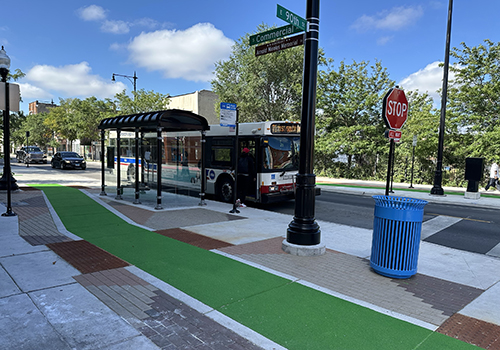 Green-painted bike lane at sidewalk level on the outside of a bus shelter with a CTA bus stopping in the street