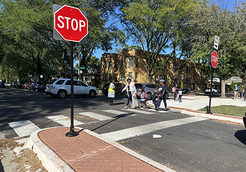 crosswalk at stop sign with detached concrete bumpouts and a group of adults and kids crossing the street