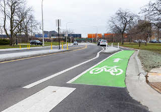 A person rides a bike in a bike lane between the curb a parking lane with concrete barrier separation