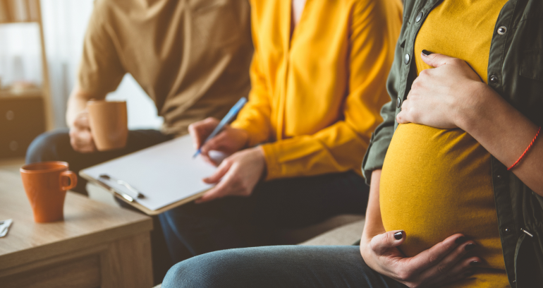 Pregnant woman sitting on couch with person who has clipboard